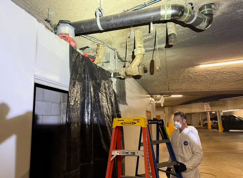 Plumber in protective coveralls and mask with plastic sheeting protecting a garage floor