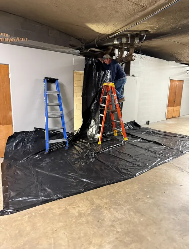 Plumber on a ladder replacing overhead drain lines in a commercial parking garage