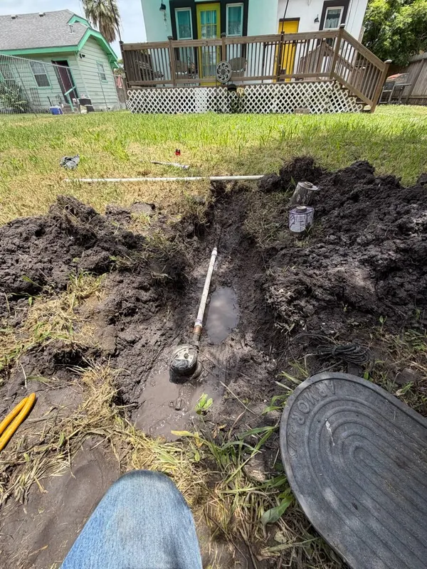Open trench dug across a front yard exposing a sewer line and cleanout