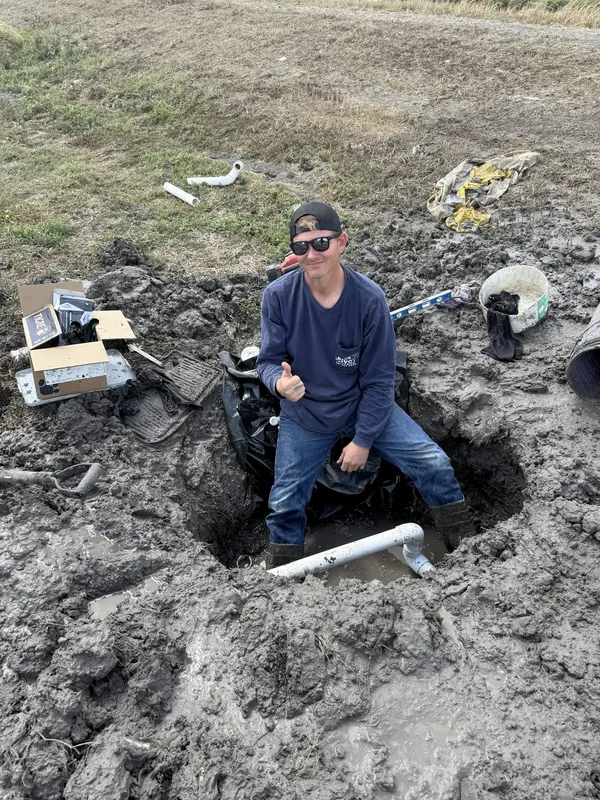 Plumber in a dug hole repairing a main sewer line in a field