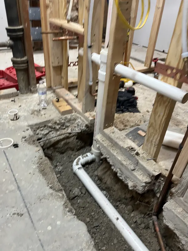 New PVC drain and vent lines roughed into a cut concrete slab and stud wall