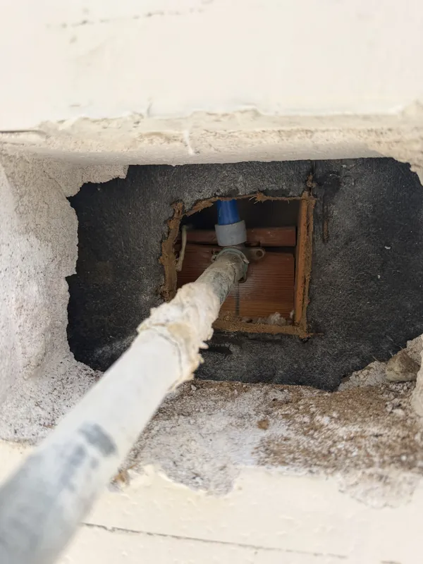 Access hole opened in a stucco wall exposing a supply line for repair