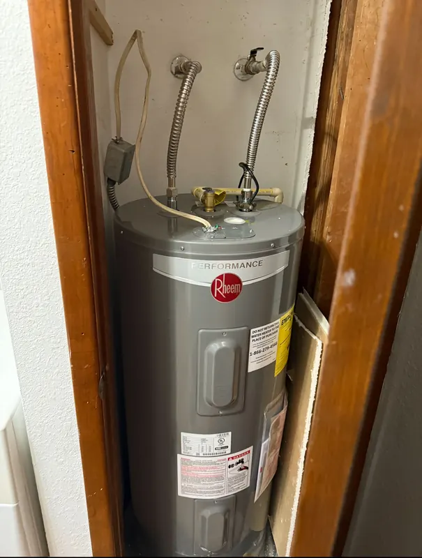 New Rheem electric water heater installed in a closet with braided supply connectors