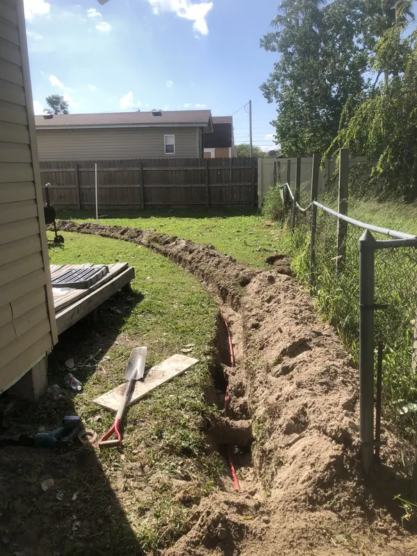 Hand-dug trench along a backyard fence with a new line laid for a house
