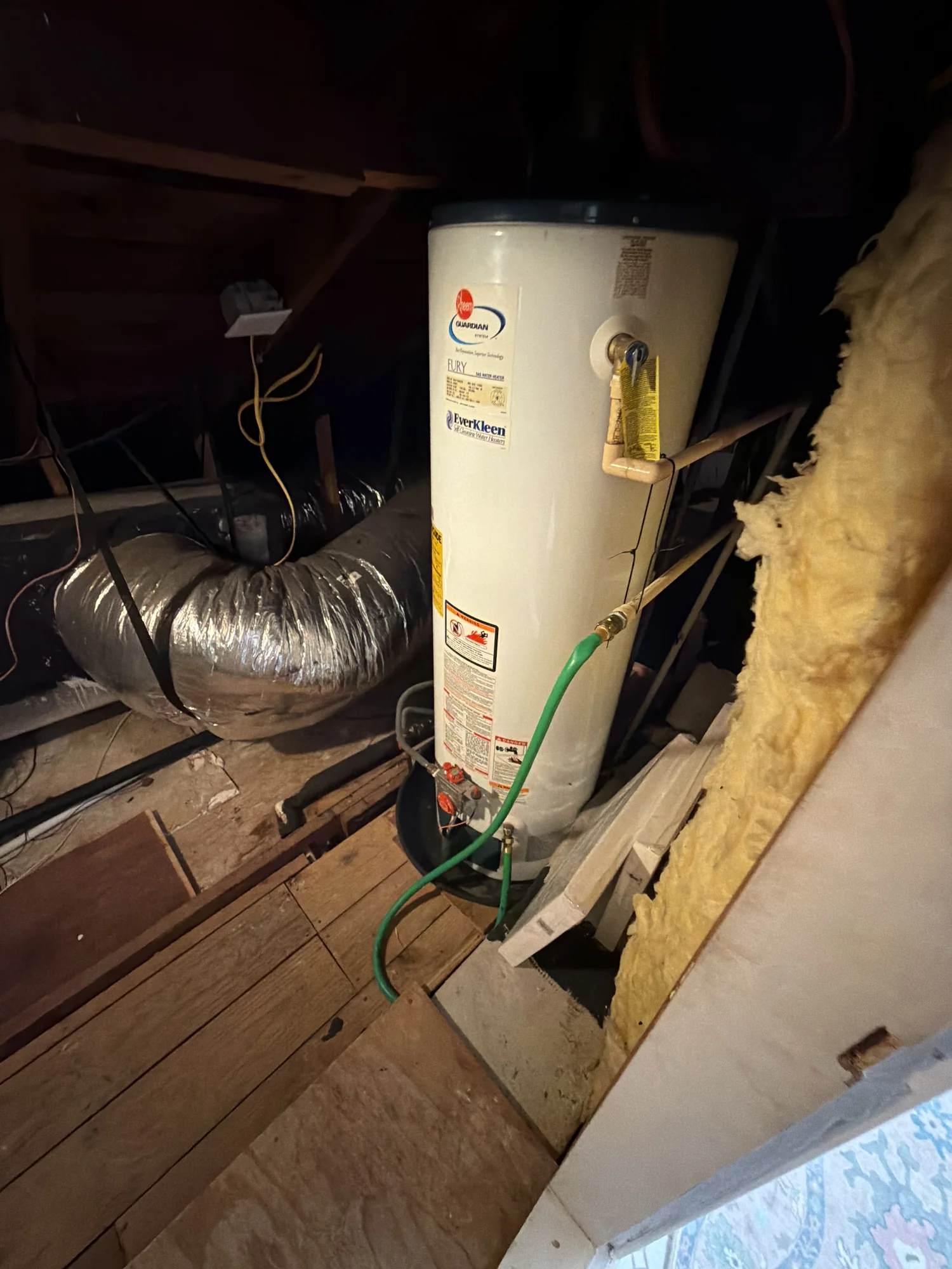 Old cracked white Rheem Guardian water heater in an attic before replacement